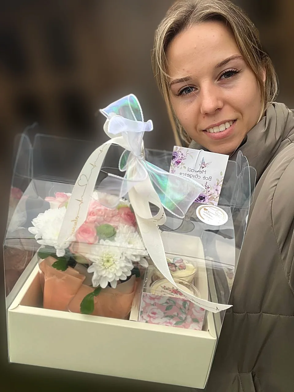 Девушка держит подарочный набор: цветы и трайфлы в коробке с бантом